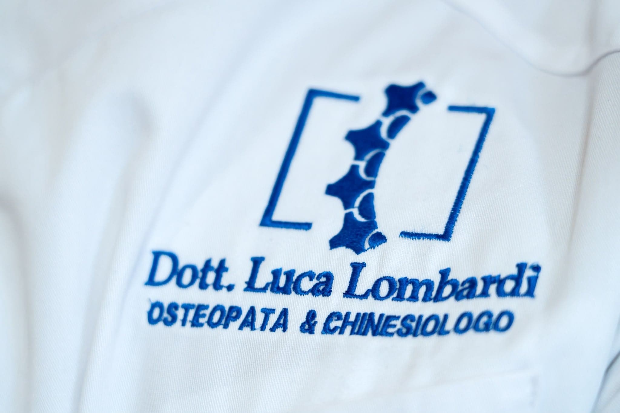 Dettaglio della divisa bianca con il marchio ricamato in blu di Luca Lombardi, Osteopata & Chinesiologo